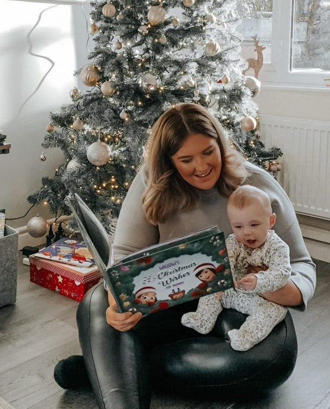 A mother and child read a personalized xmas book together next to a Christmas tree.