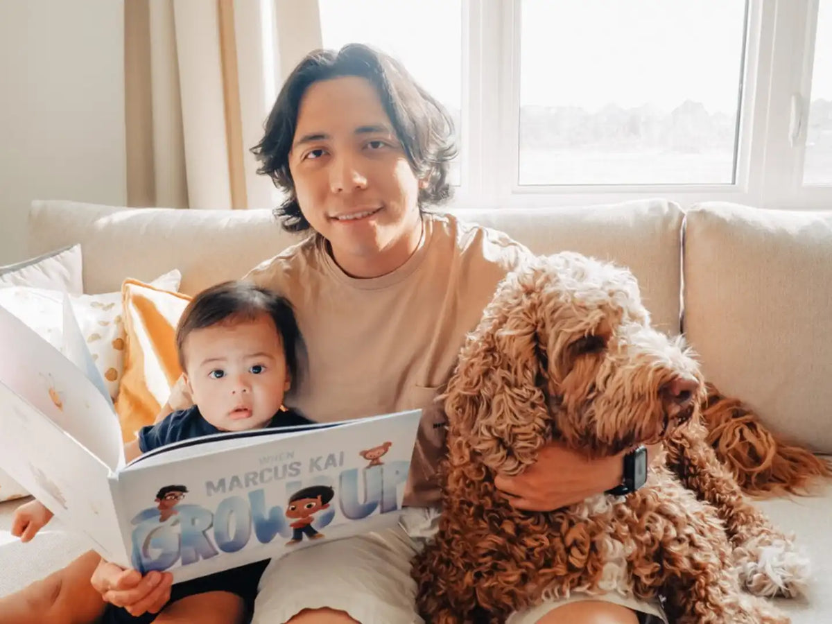 Man lovingly holding his little son and their dog reading an emotional book about what his son is going to be when he grows up.