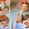 Little girl in floral dress pointing to the cover of a personalized storybook for mom and her kids.