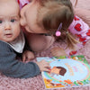 Girl kissing her little brother, with a personalized book about healing after loss lying beside them.