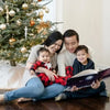A happy family is reading the personalized book for siblings with their two kids beside the Christmas tree.
