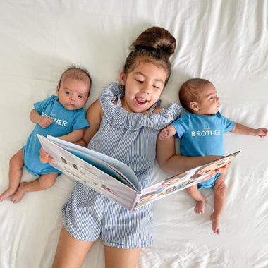 A big sister reads her baby twin brothers a customized treasure hunt book all about their adventures.