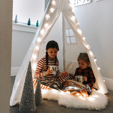 Two sisters sit in a tent drinking tea and reading their sibling Christmas book.