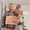 A couple smiles in front of an Xmas tree with their own custom couples' book for him, an amazing gift for boyfriends.