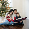 A family of four reads a personalised Christmas book together next to their Xmas tree.