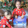 Two children in matching Xmas pyjamas admire their new Christmas book for siblings.