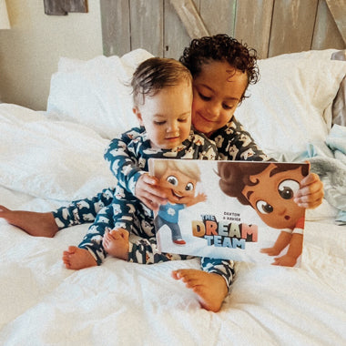 Kids sitting on a bed holding their personalized adventure book for two. 