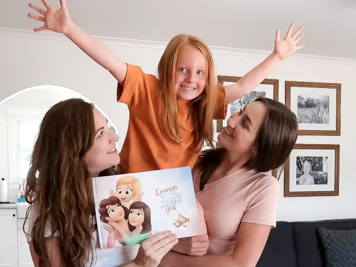 Moms and their daughter smiling and holding their personalized book.