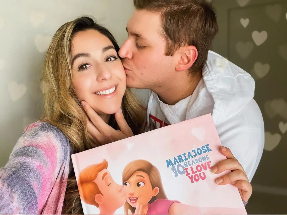 A man is kissing his girlfriend who just got her personalized love book for couples which is a great Valentine's Day gift.