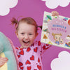 Happy girl proudly holding her personalized present, a book about becoming a big sister, after welcoming her baby brother.
