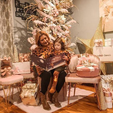 Mother and child sit together next to their Christmas tree reading a personalized Xmas book.