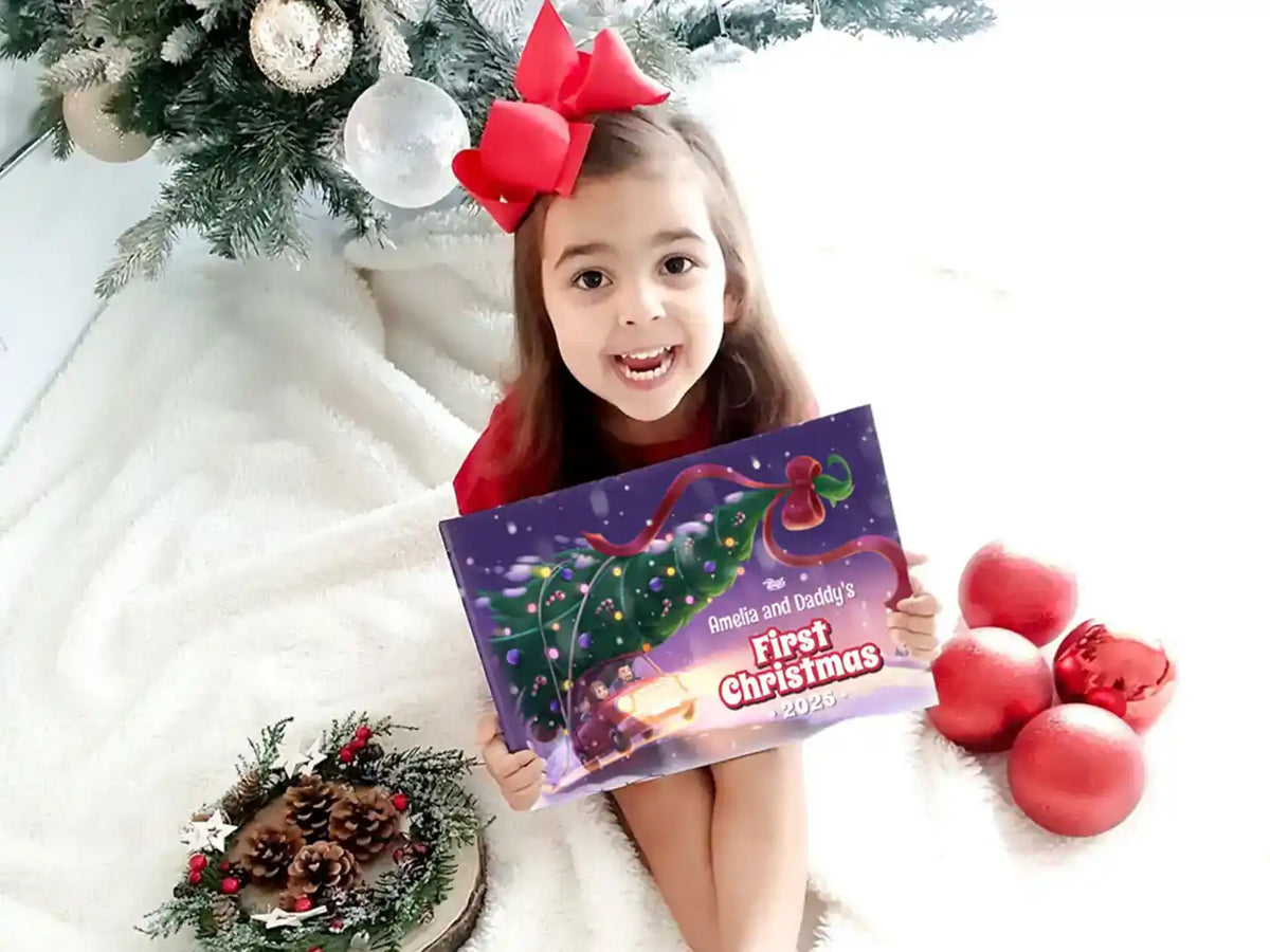 Girl holding a personalized “First Christmas 2025” book with her name on the cover.