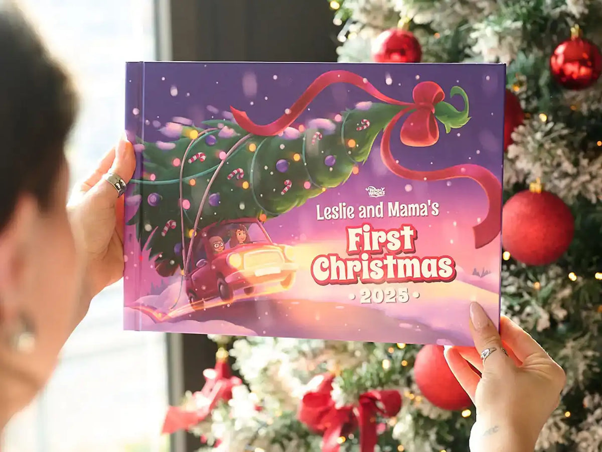 Hands holding a personalized Christmas book titled “Leslie and Mama’s First Christmas 2025” next to a decorated tree.