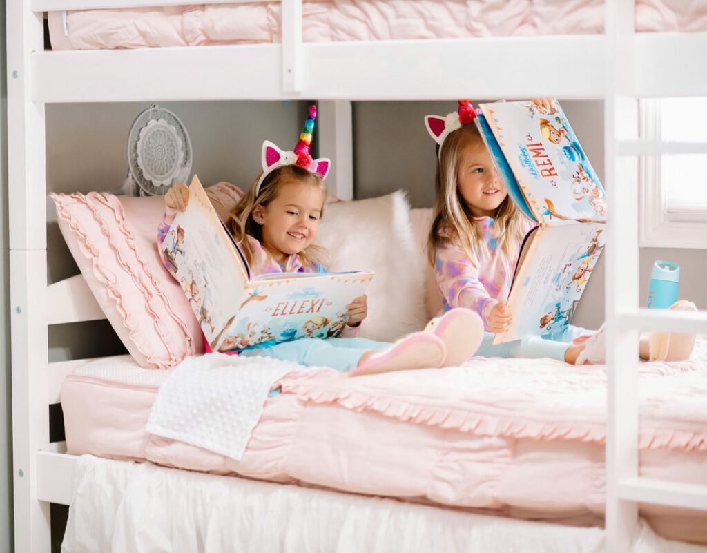 Two little girls sitting on the bed reading their own personalized birthday book from Hooray Heroes