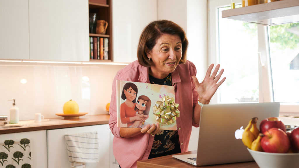 A grandmother, proudly showing her personalized book for grandparents from Hooray Heroes on a video call.