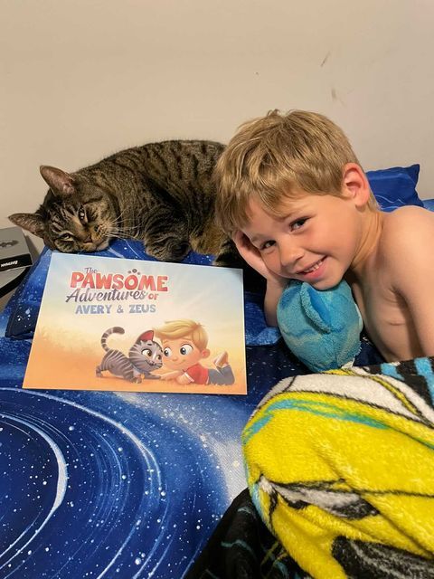 A little boy sits on the couch with his cat and their personalized book for pets.