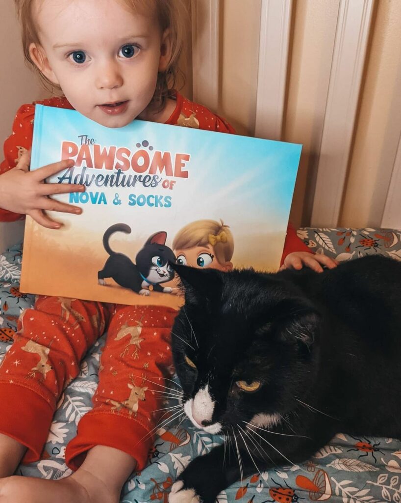 A little girl holds a customized book for her and her cat with her cat sitting nearby.