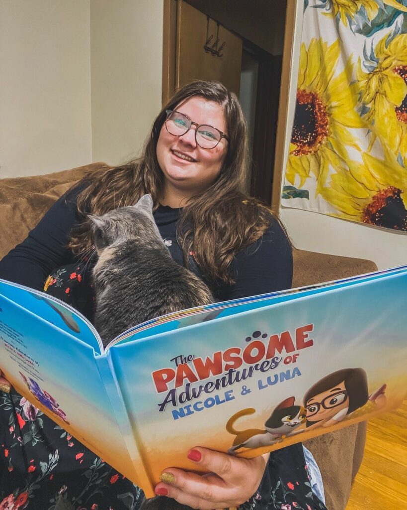 A woman sits with her cat and their custom, one-of-a-kind book for her and her kitty.
