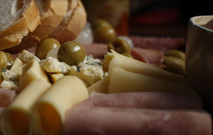 A plate covered in assorted deli meats, cheeses, olives and bread.