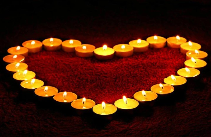 A number of lit tea lights laid out in the shape of a heart. 