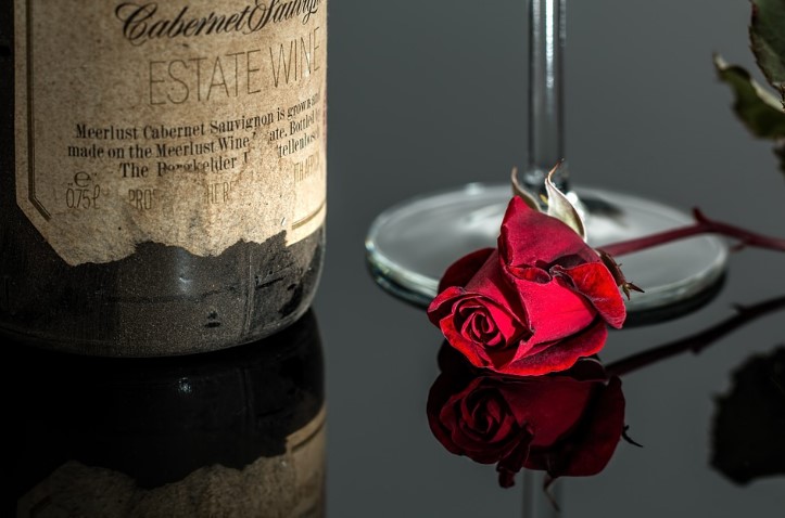 A vintage bottle of wine on a table with a glass and a single rose.