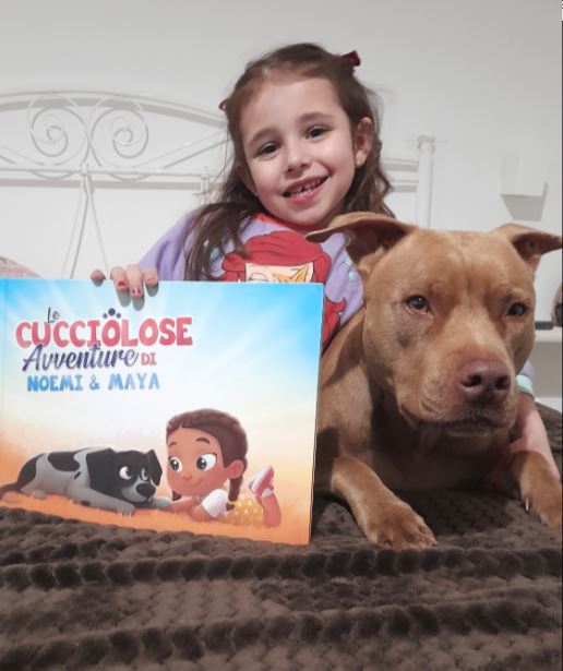 A little girl called Noemi with her dog, holding a personalized book for kids and pets from Hooray Heroes.