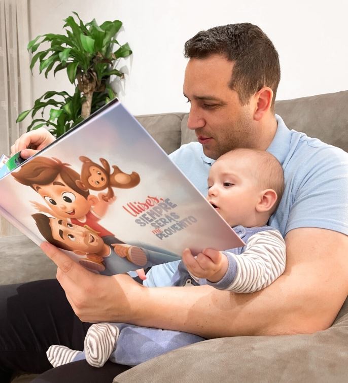 A baby boy named Ulises, reading a personalized book from Hooray Heroes with his dad.