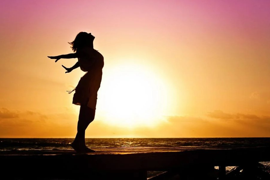 The silhouette of a woman standing on the beach with a sunset behind her.