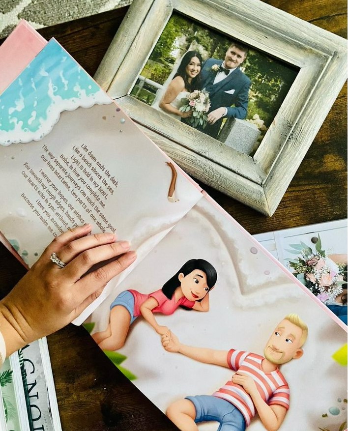 A woman's hand holds open a personalised love you book next to her wedding photo. 