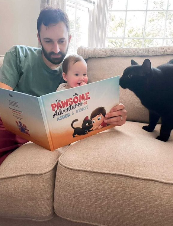 A baby boy, his dad and their cat with a personalized book for pets and kids from Hooray Heroes.