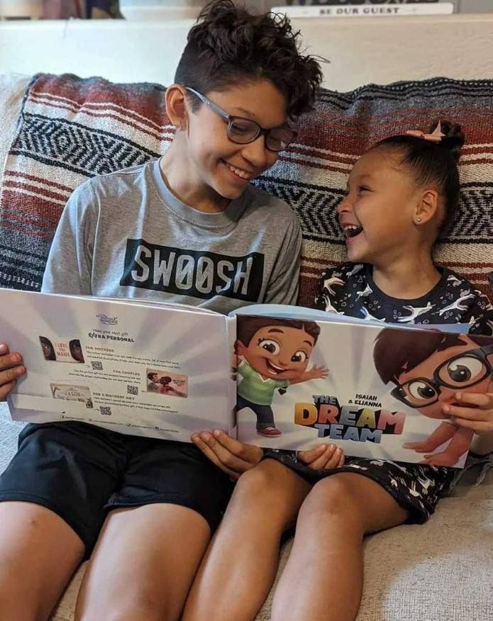 An older brother and younger sister sit together on the couch to read their own customized book for friends, cousins, or siblings, the best xmas gift.