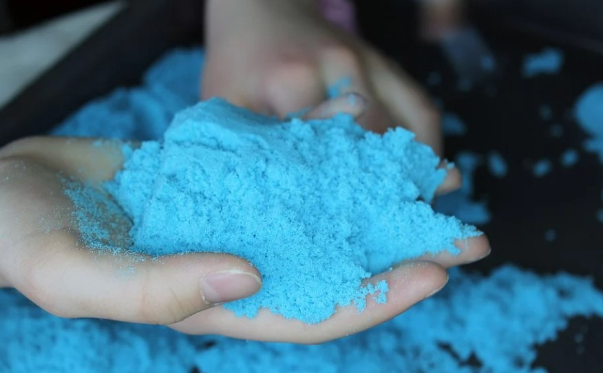 A child with hands full of blue kinetic sand.