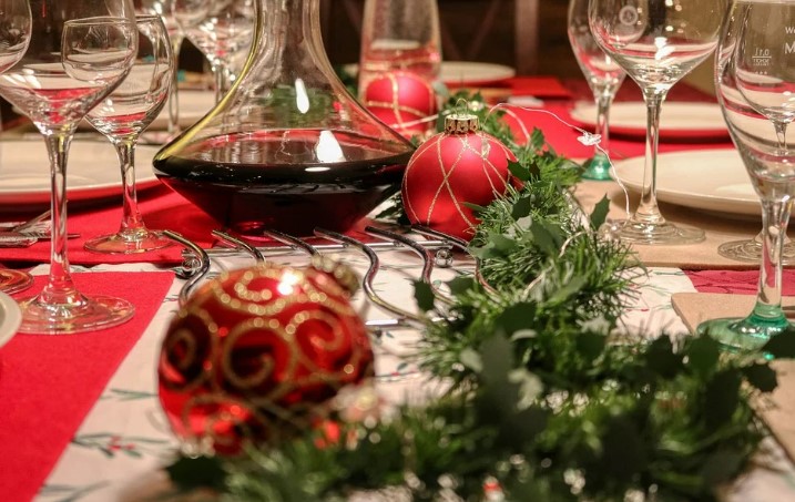 A Christmas table set with wine and wine glasses, greenery and red decorations. 