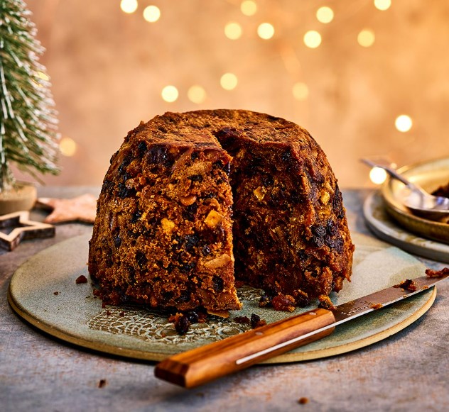 A beautifully steamed British Christmas pudding on a tray with a piece already missing.