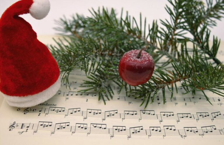 A santa hat rests on sheet music next to some winter foliage and an apple.