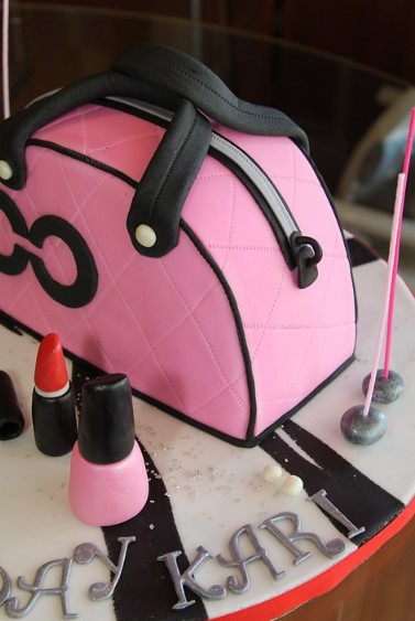 A cake that was made to look like a pink purse, lipstick, and nail polish. 