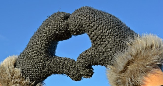 Someone wearing mittens making the shape of a heart with their hands. 