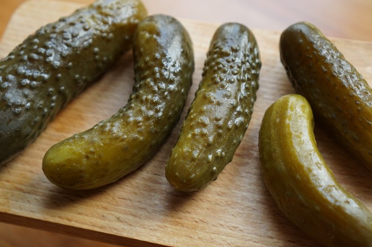Five pickles on a wooden cutting board. 