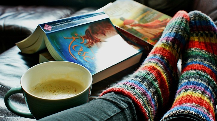 Someone with colorful warm socks on their feet next to an open book and a cup of coffee.